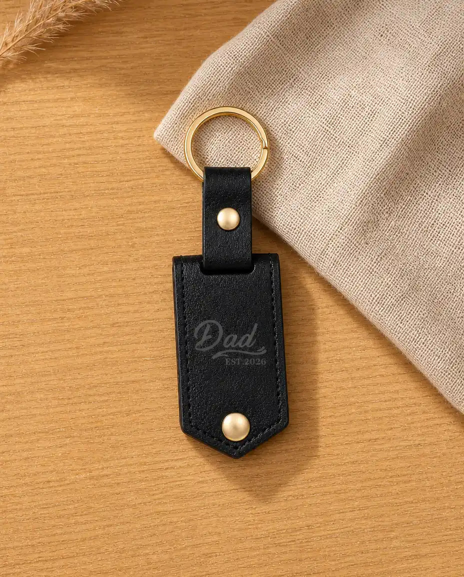 Personalised black leather photo keyring engraved with Dad Est. 2026 on a warm wood table